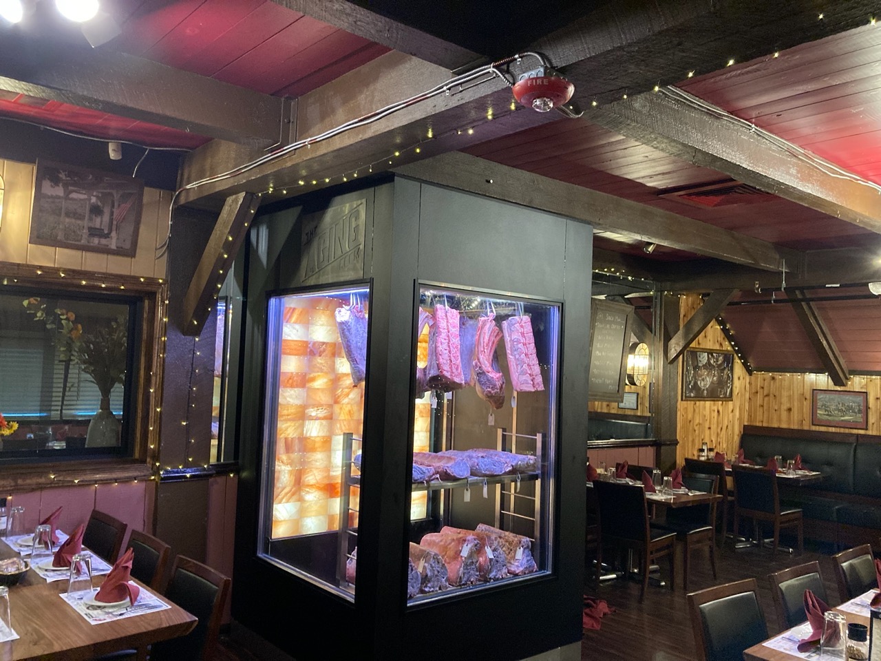 The Aging Room. Premium Meat Dry-Aging Walk-in Chamber with a Wall of Pink Himalayan Salt. Dry-aged meat cuts laying on the shelves and hanging.