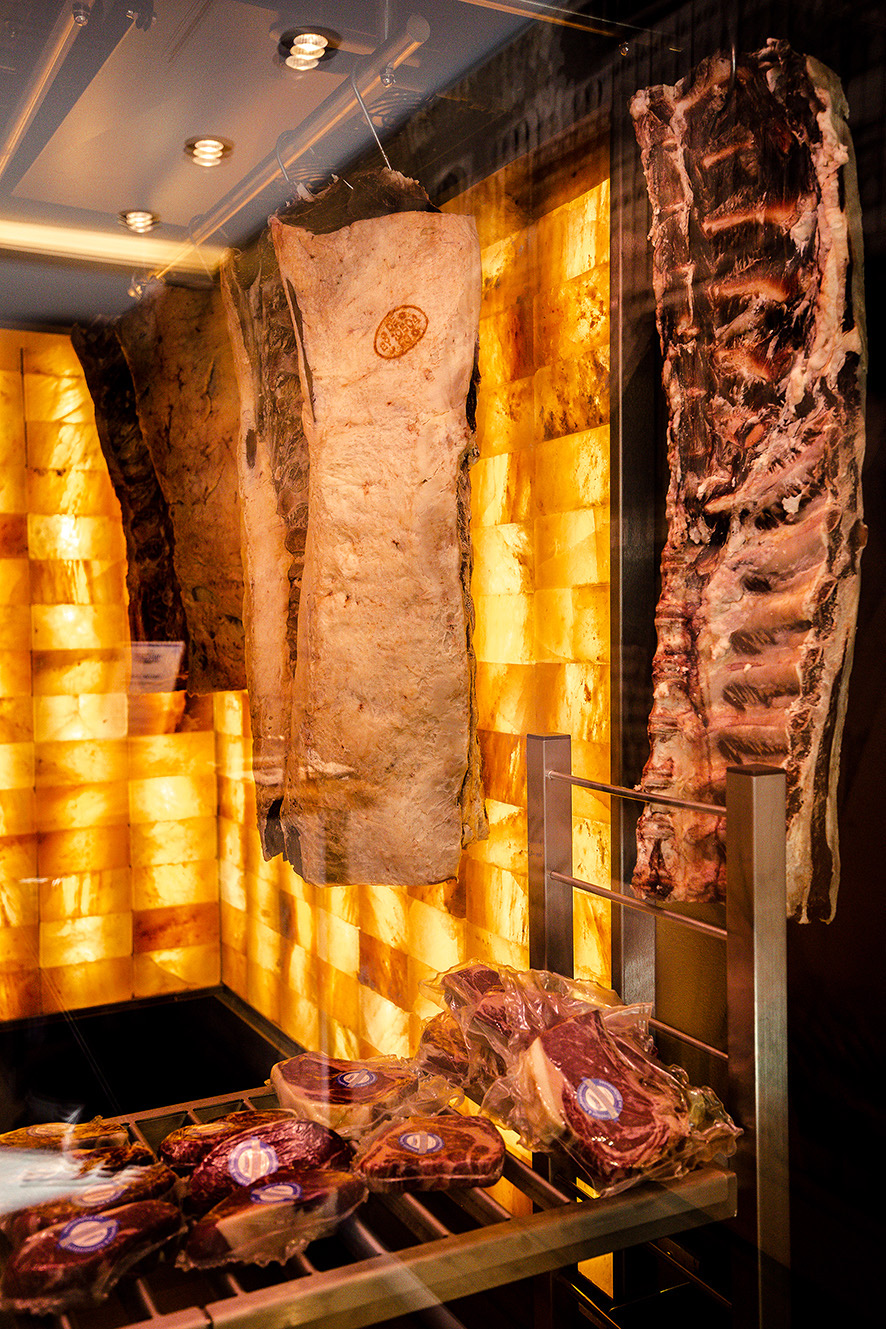 TAR. The Aging Room for Meat Dry-Aging. Pink Himalayan salt wall in a walk-in Dry Aging Chamber. Dry Aged Meat hanging on the hooks and Dry-Aged cuts laying on the shelves inside a Dry-Aging Cabinet.