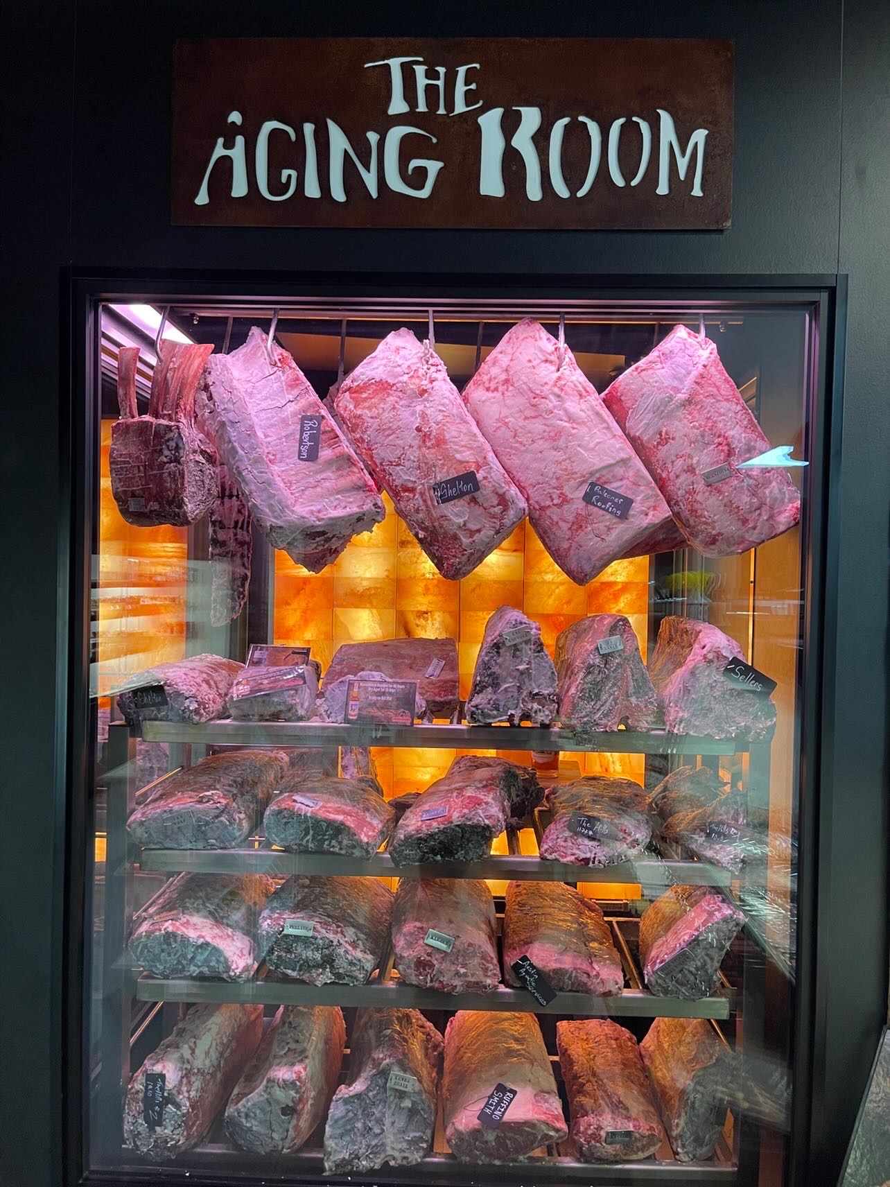 Dry Aging Chamber with a wall of real pink Himalayan Salt. Dry-Aged meat laying on the shelves and hanging on the hooks.