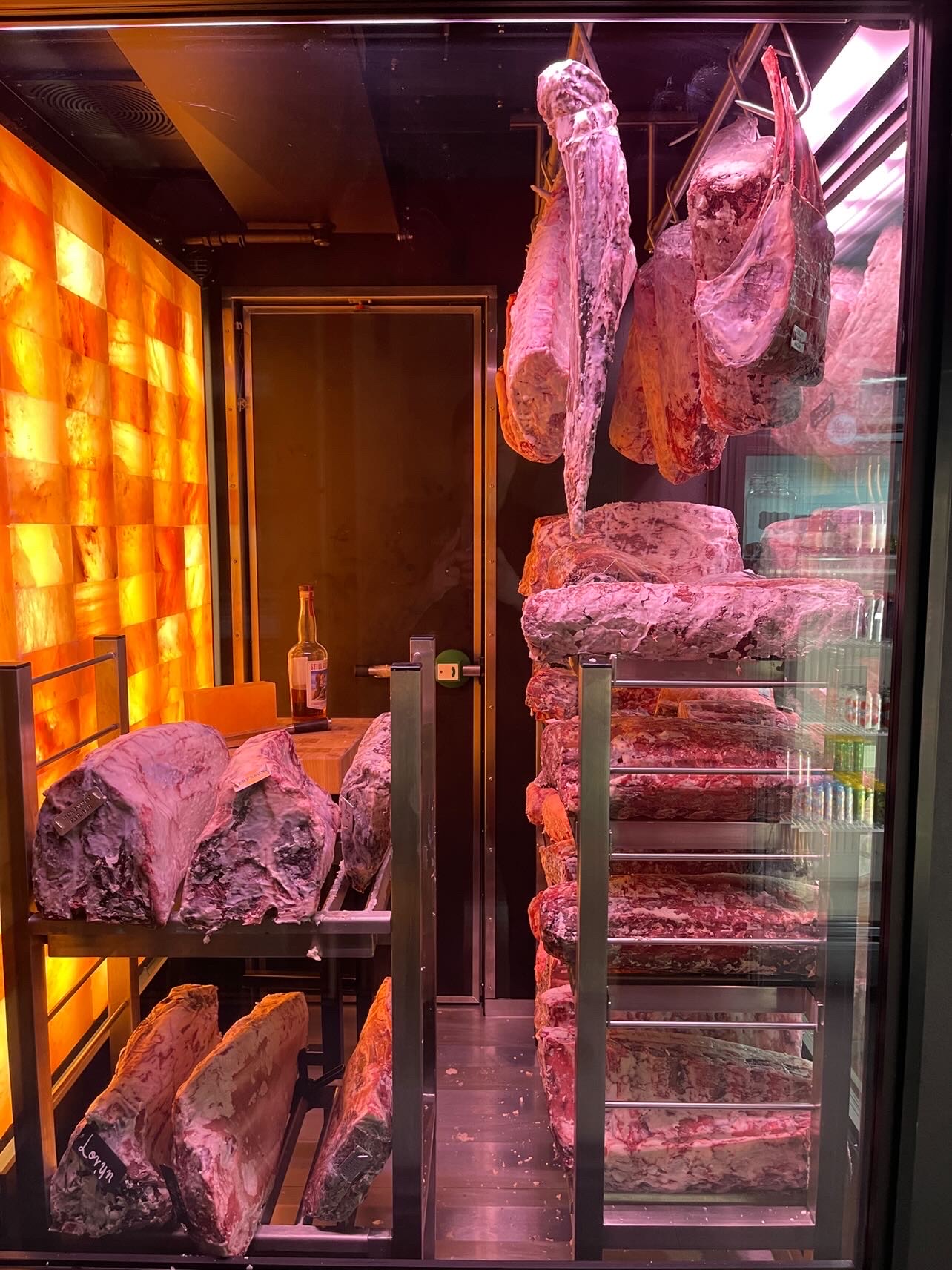 Dry Aging Chamber with a wall of real pink Himalayan Salt. Dry-Aged meat laying on the shelves and hanging on the hooks.